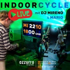 Hinweis auf ein Cycle-Special mit Live-DJ: Ein junger DJ legt im bunten Scheinwerferlicht Musik auf. Im Vordergrund sind Sportlerinnen auf Spinbikes zu sehen.